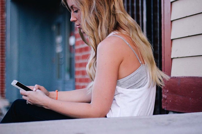 Ein blondes Mädchen mit langen Haaren benutzt ihr iPhone für Support